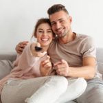 cheerful loving couple sitting on couch together and watching tv